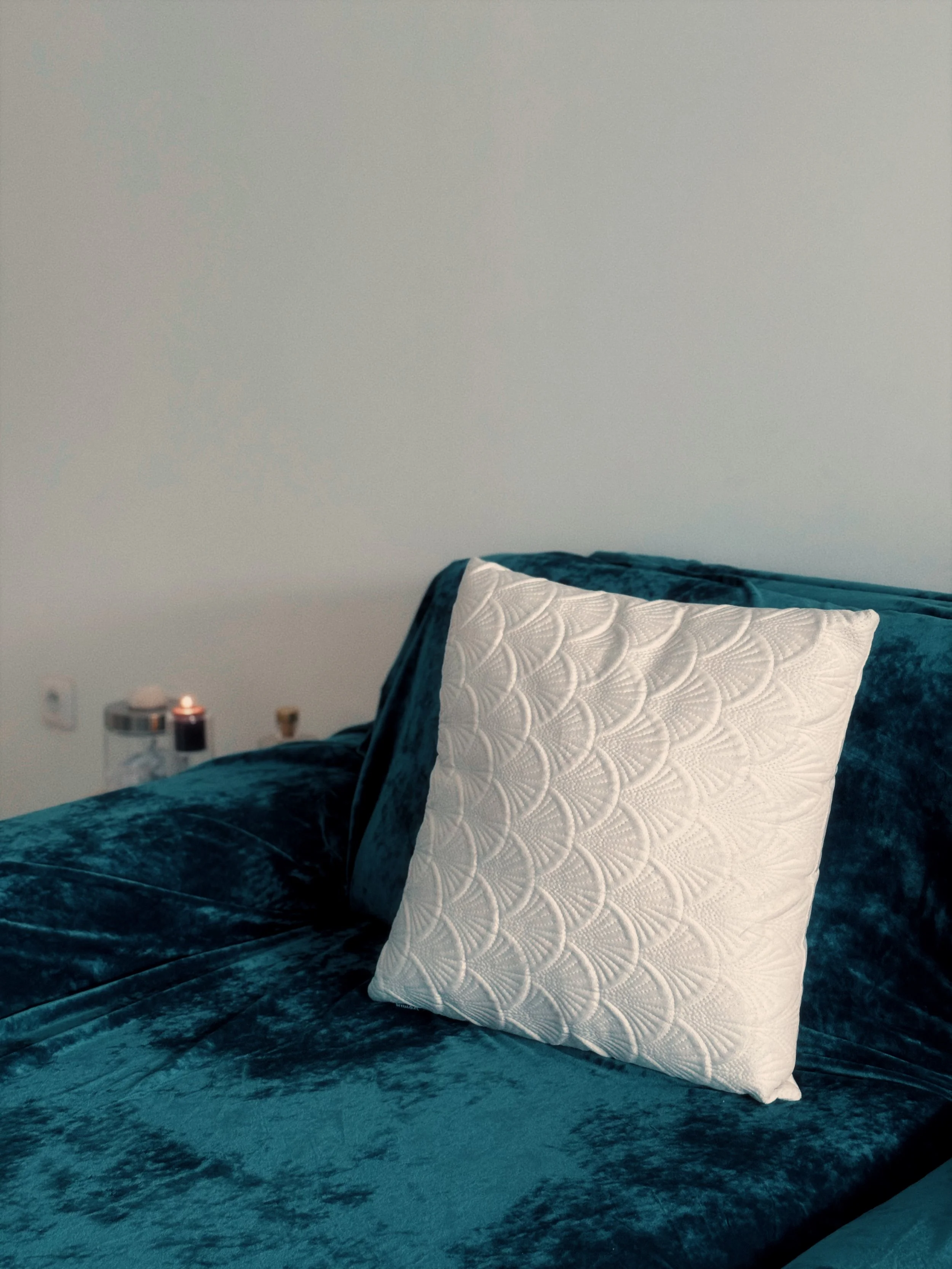 Un lit avec une couverture en tissu bleu et un oreiller blanc avec un motif en relief, dans une chambre minimaliste
