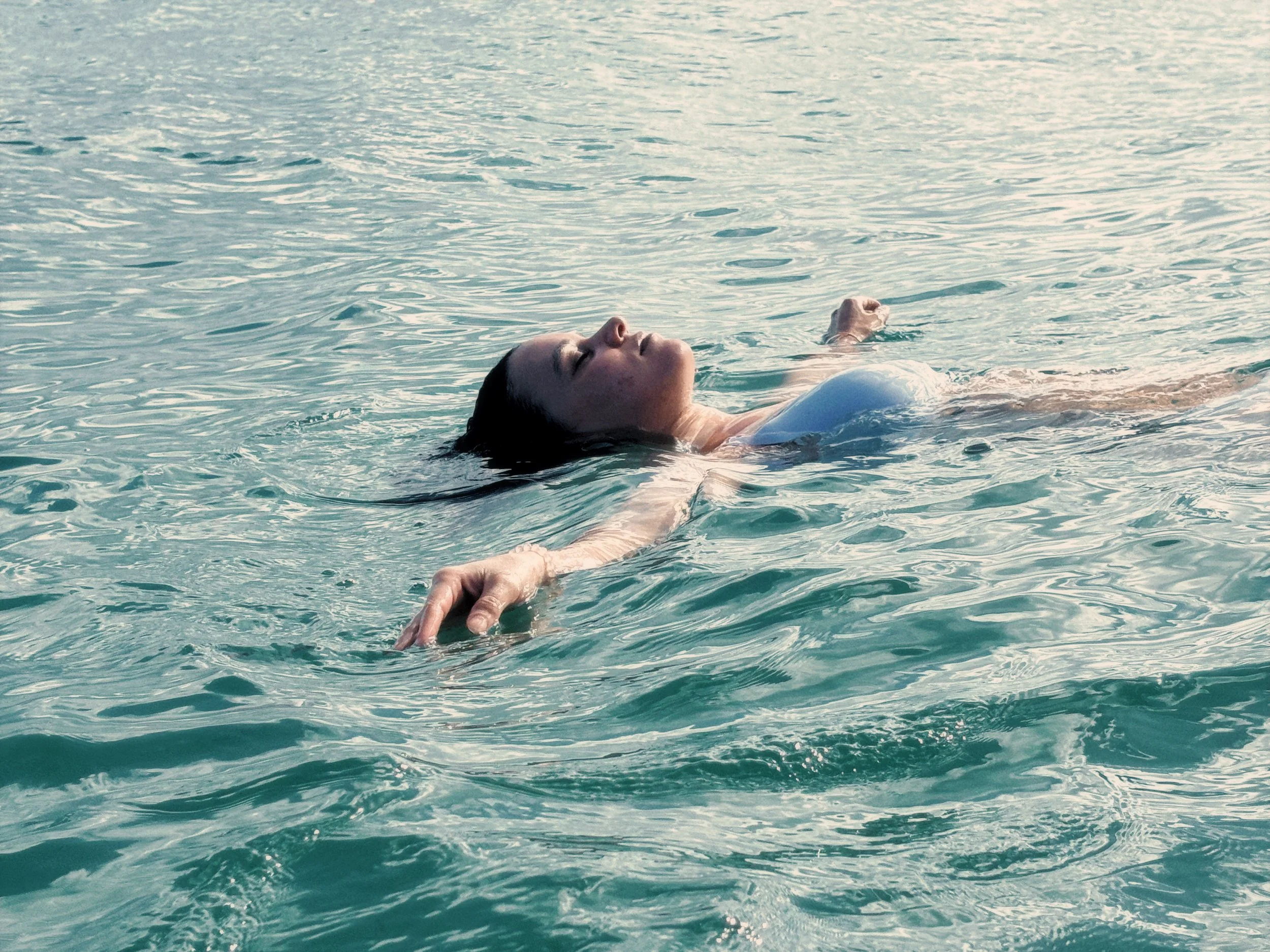 Une femme nage seule dans une mer calme, face à un horizon sans horizon visible.