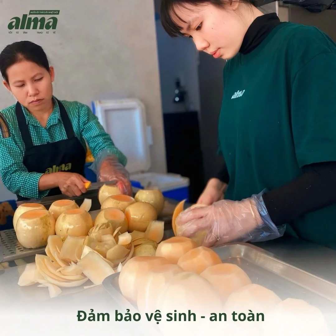Two women peeling onions in a food preparation area. One woman is wearing a green checkered shirt and apron, and the other woman is wearing a green shirt. They are working with peeled onions on a table, emphasizing hygiene and safety.