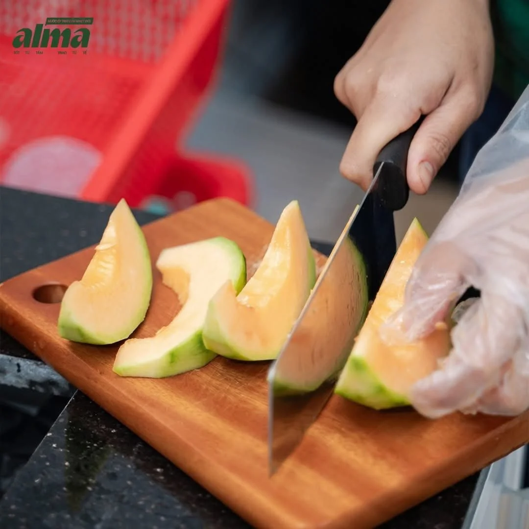 Person slicing cantaloupe melon on a wooden cutting board in a kitchen.