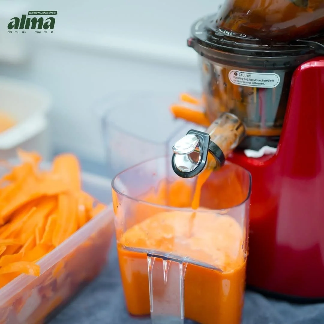 Orange juice being prepared with a juicer, with a container of sliced oranges nearby.