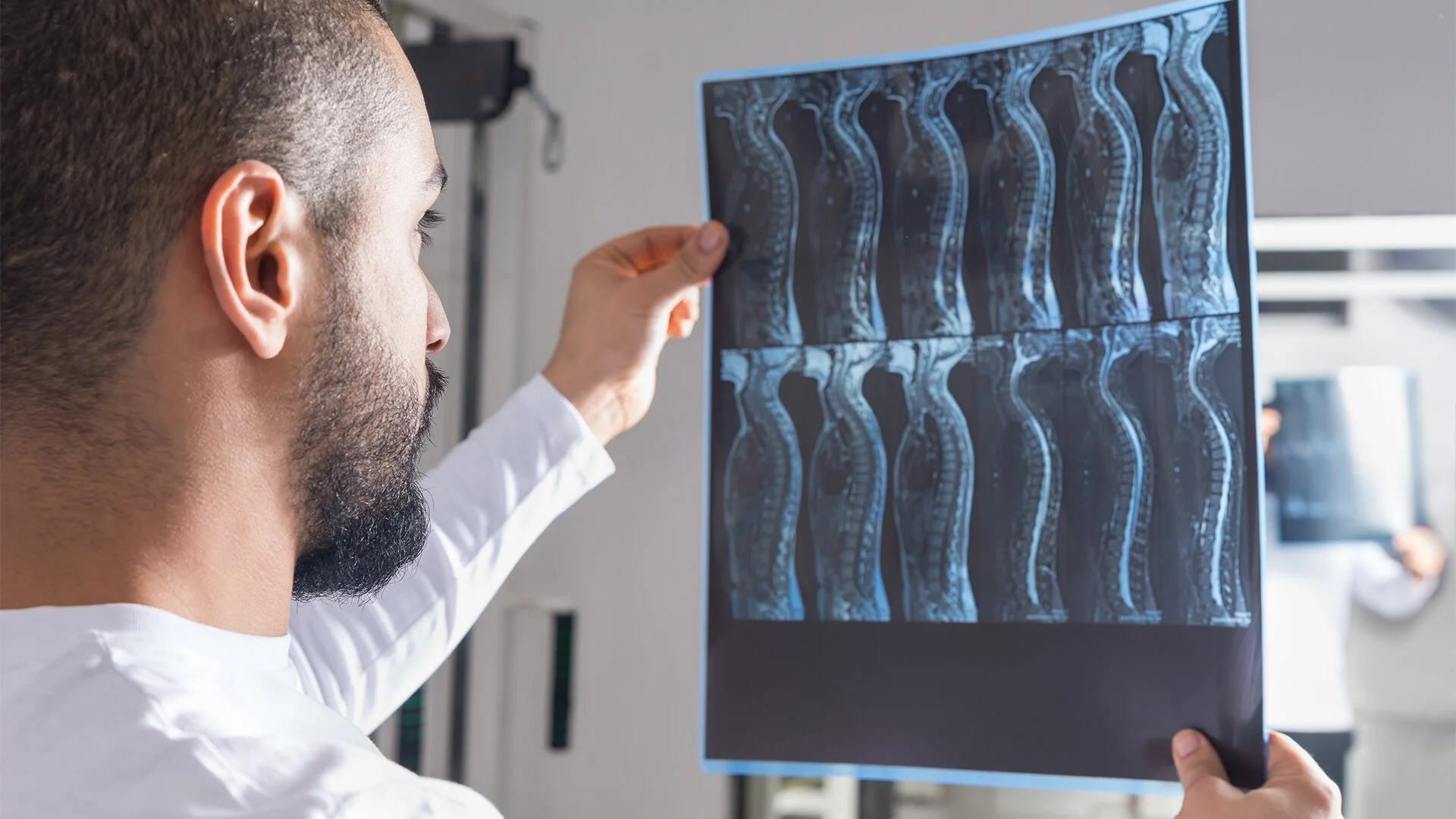Medical professional examining spinal MRI scan on lightbox in a clinic or hospital setting.