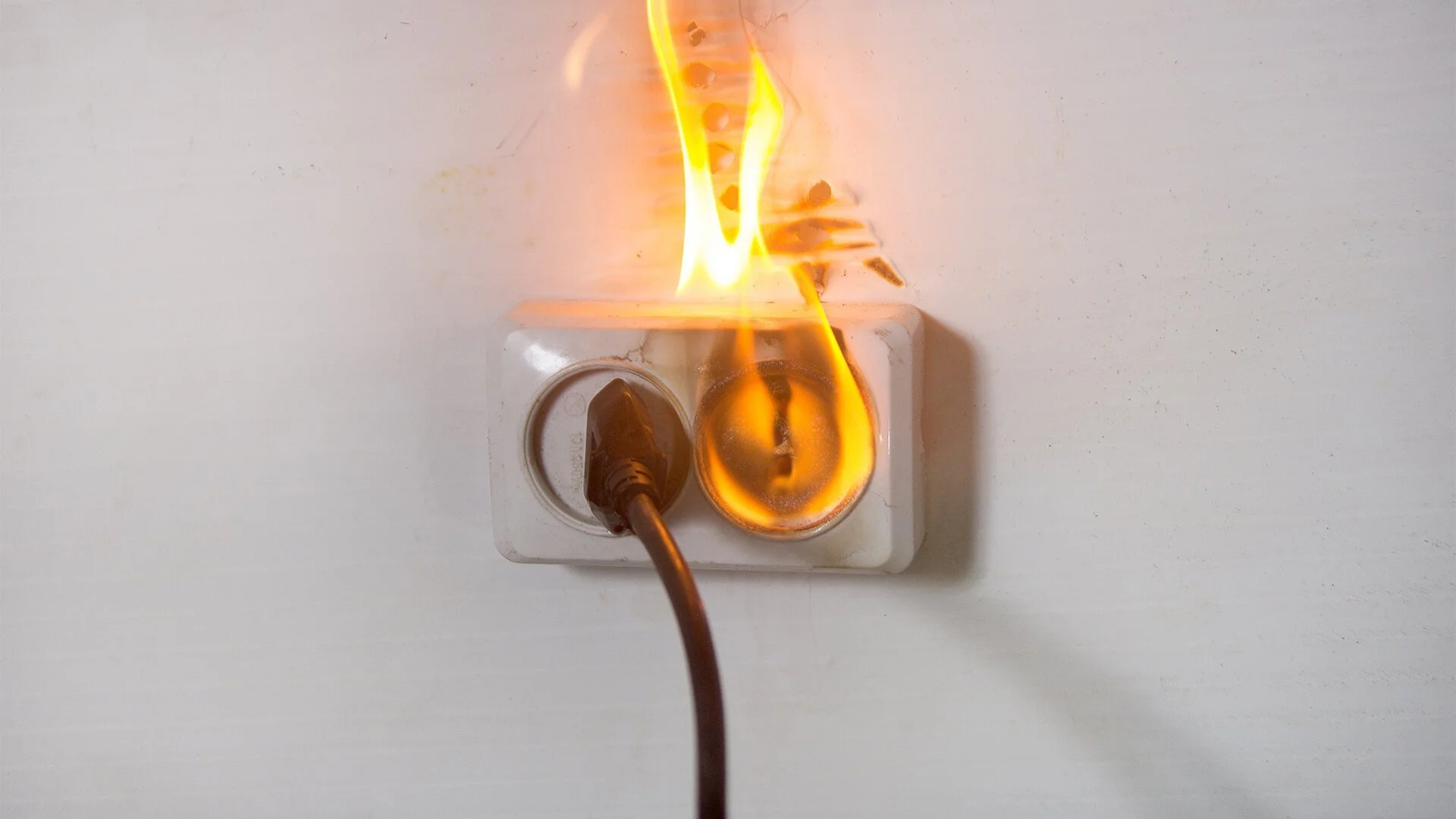 Electricity plug in a wall socket with sparks and flames.