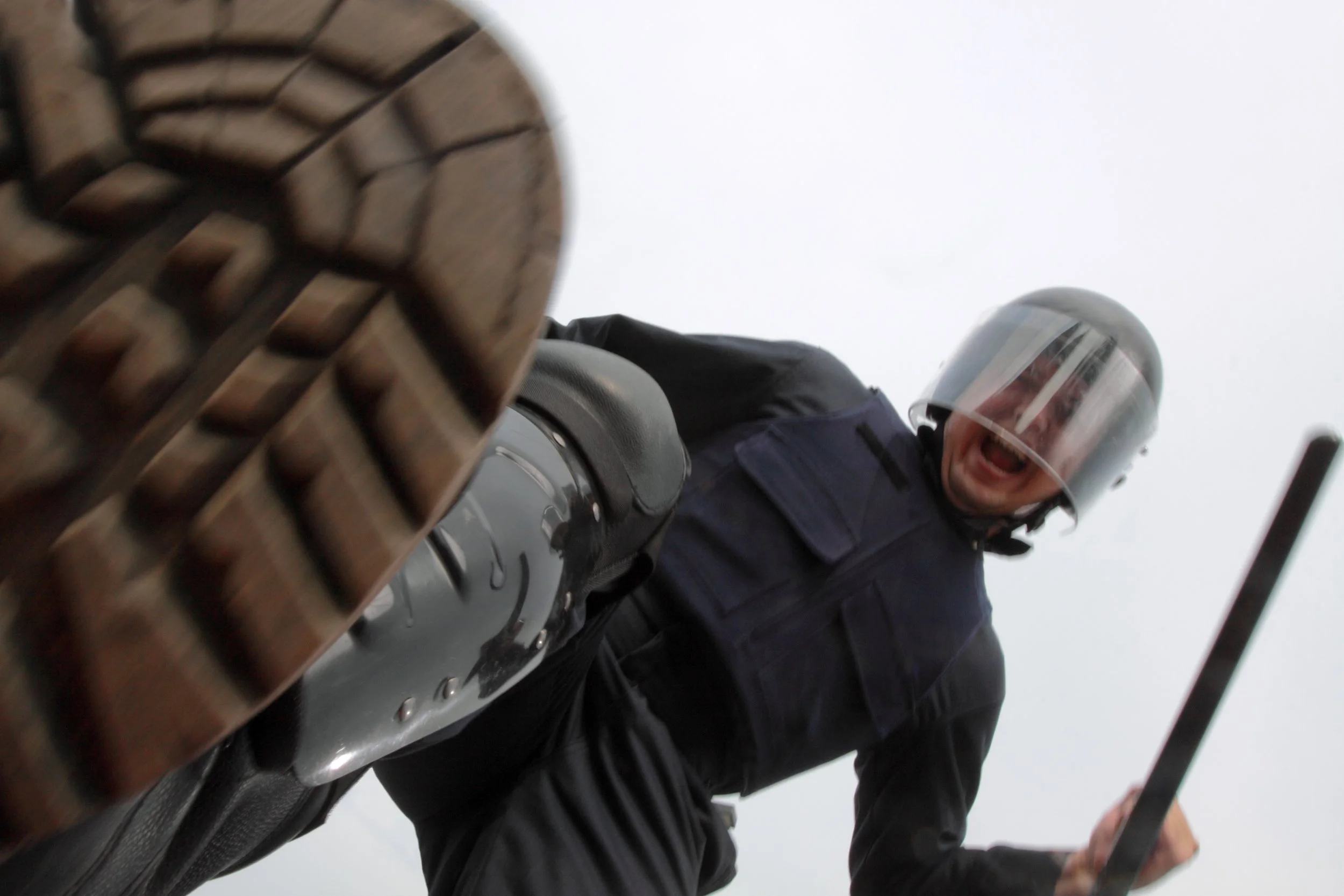 A person wearing a helmet and black jacket, riding a motorcycle, looking down, with the view from below the motorcycle's front tire.