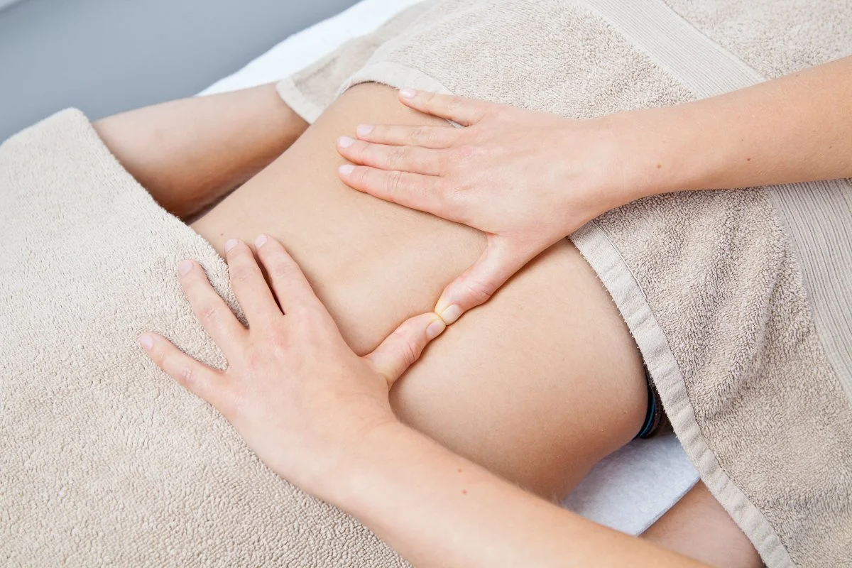 Hands of a therapist performing Bowen Therapy moves on the lower back of a client, which is partially covered by a beige towel.