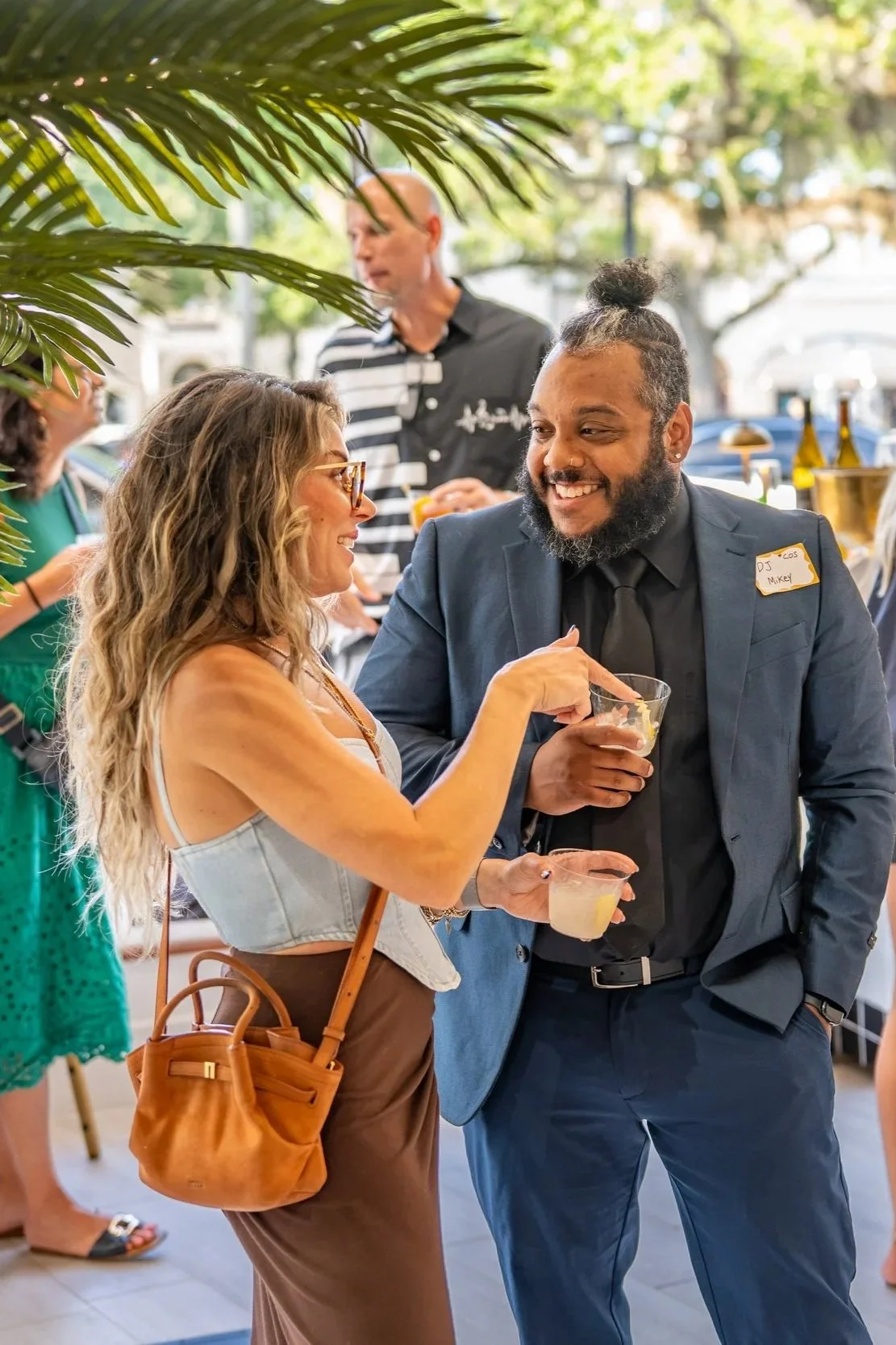 People socializing inside a cafe, with one man and woman smiling and holding drinks, while others are in the background near a counter.