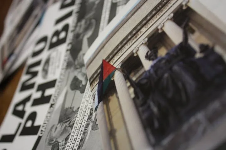 Close-up of a newspaper headline, a small flag on a building, and part of a classical building facade with columns.