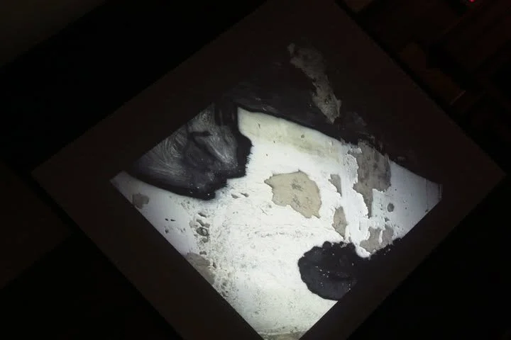 Close-up of peeling and damaged paint or plaster on a wall with dark shadows.