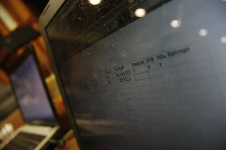 Close-up photo of a computer screen displaying a spreadsheet with columns labeled 'Email', 'Saadat SF9', 'Asad Bittah', containing email addresses and checkboxes.