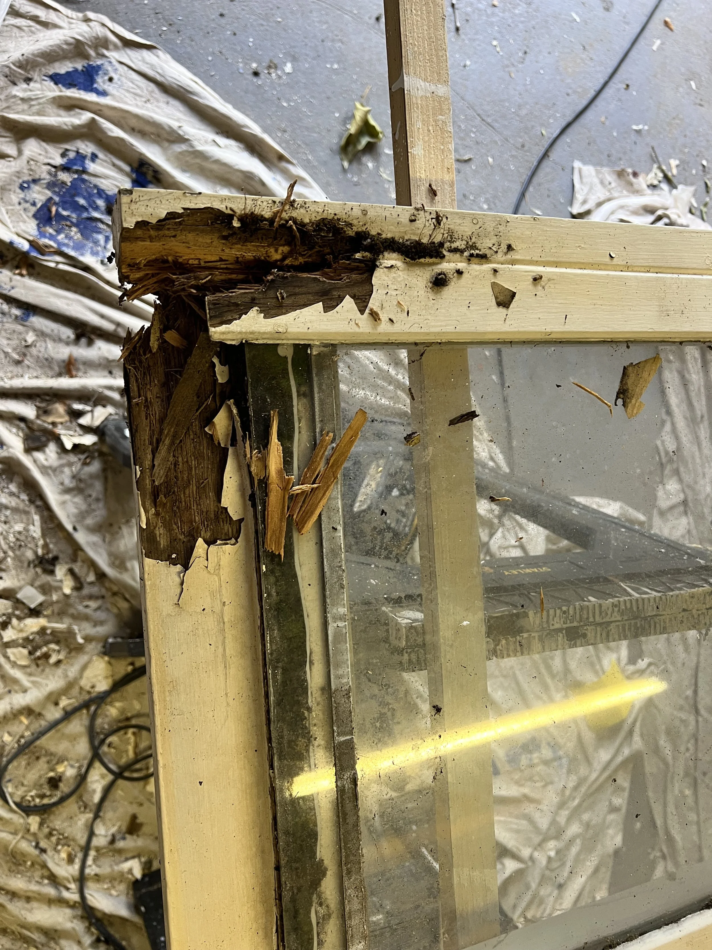 Close-up view of a damaged wooden frame with broken and splintered wood, surrounded by debris and construction materials in a workshop or construction site.