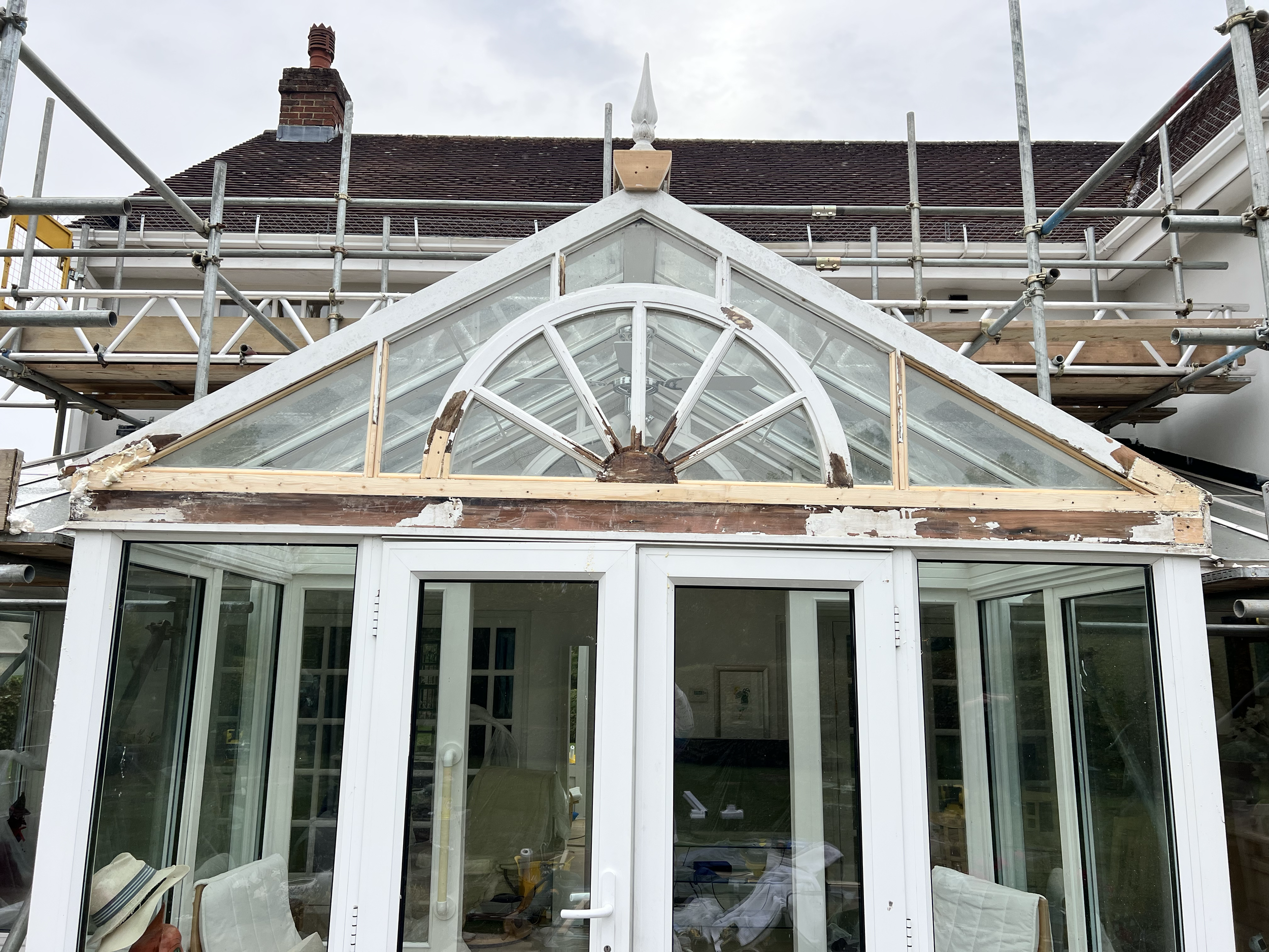 A house under renovation with scaffolding and a partially finished conservatory or sunroom with a triangular window.