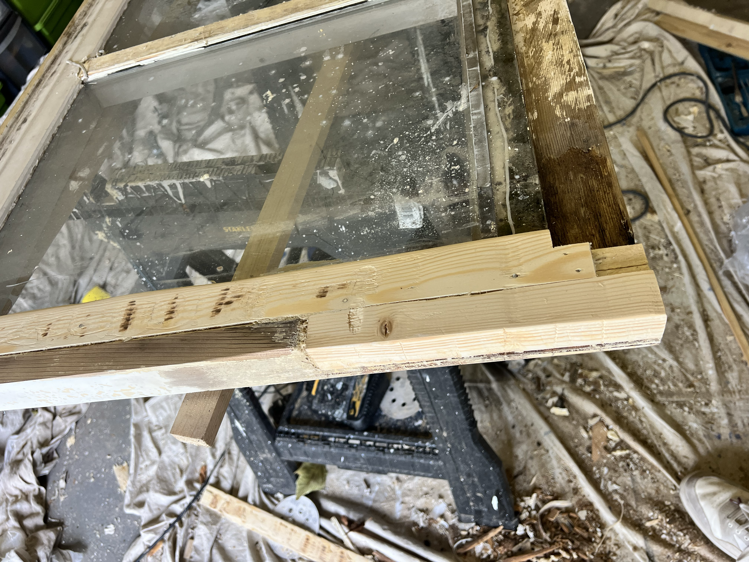 A woodworking workspace with a partially assembled wooden and glass structure, surrounded by sawdust and tools.
