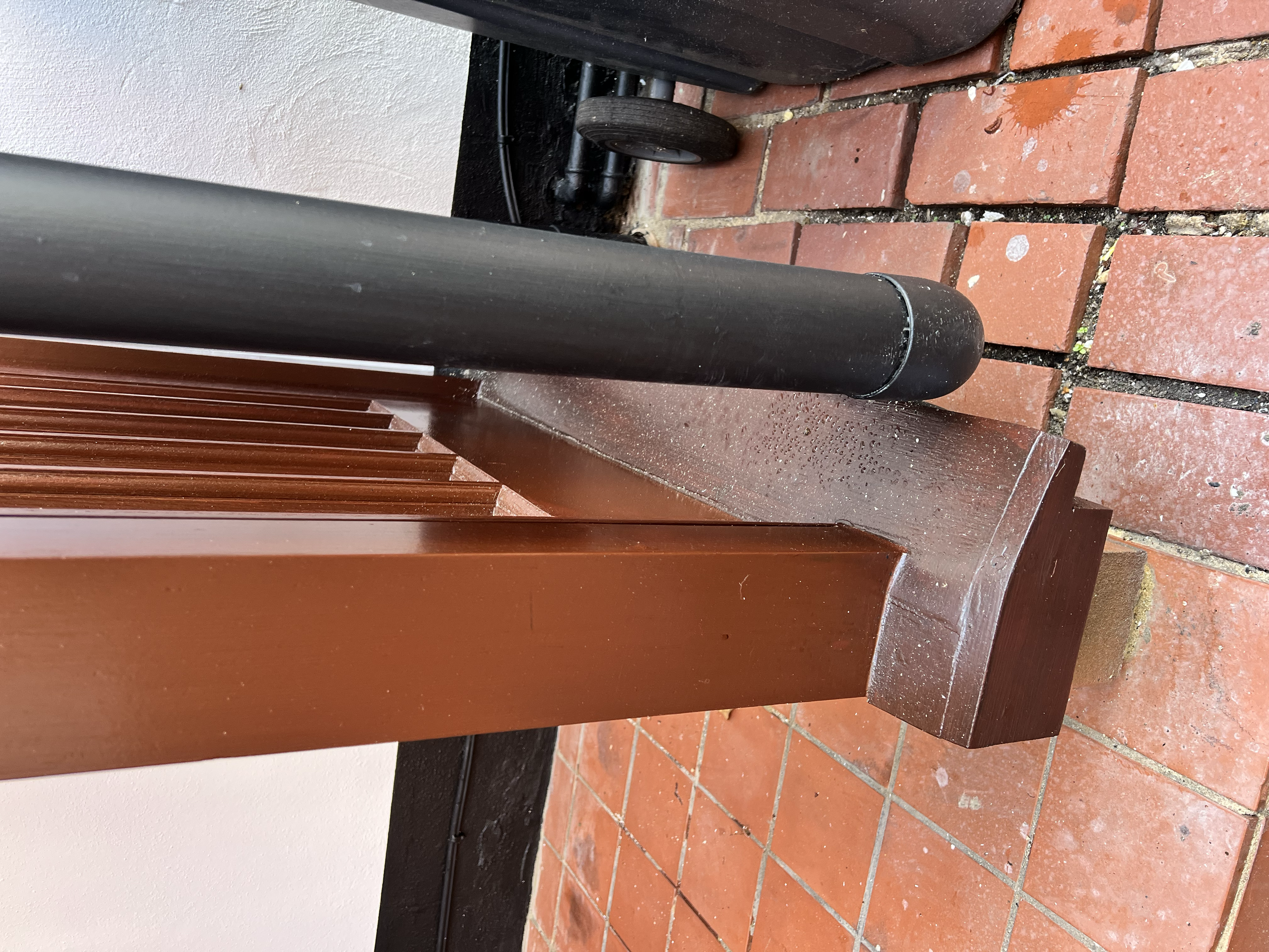 Close-up of a wooden park bench with black metal supports on a red brick pavement, with black and brown objects in the background.