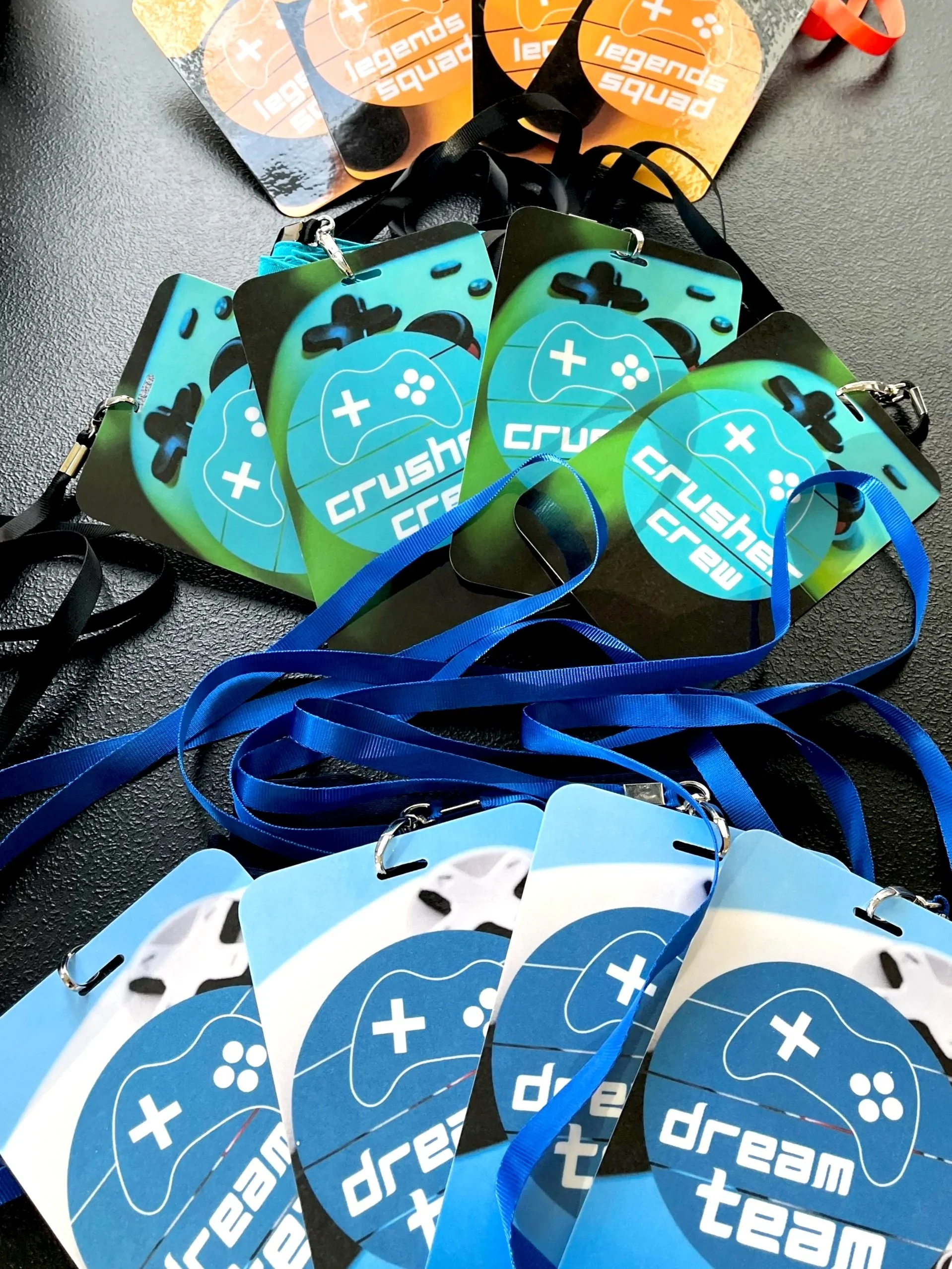 Multiple lanyards with colorful tags displaying the word 'dream team' and gaming-related graphics, arranged on a textured surface.