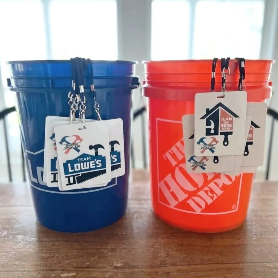Two buckets, one blue and one orange, with tags from Lowe's and The Home Depot, hanging from black lanyards on the buckets.