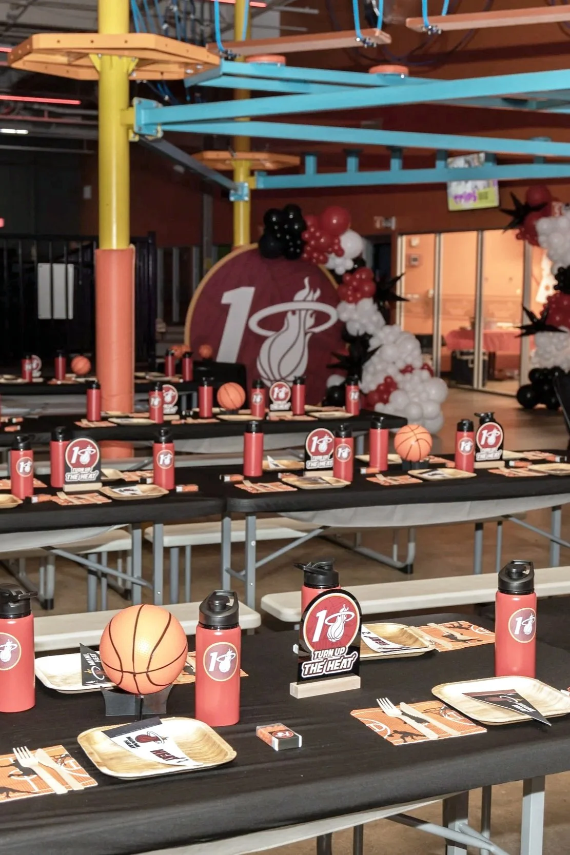 Indoor celebration setup for a Miami Heat event with balloons, themed table settings, and Miami Heat logo decorations.