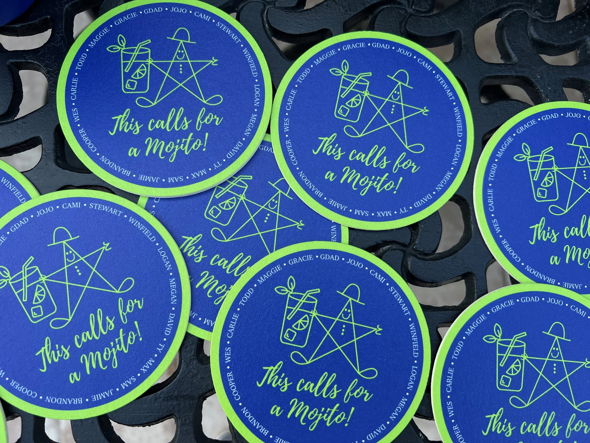Multiple round stickers with a blue background and neon green border. Each sticker features a stylized outline of a person with a sun hat, holding a drink with a straw and lemon slice, and the words "This calls for a Mojito!" written in neon green cu