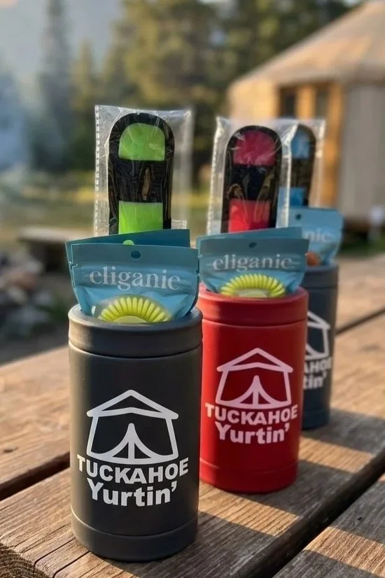 Three containers labeled 'TUCKAHOE Yurtin' with candies and hand warmers inside, outdoors on a wooden surface with trees and a house in the background.