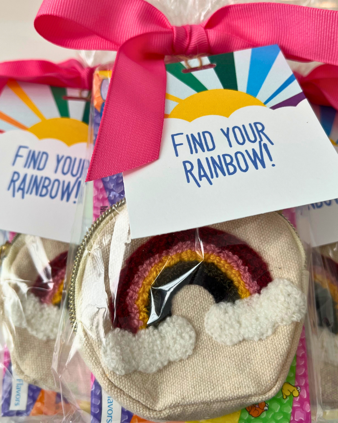 Colorful rainbow zipper accessory with clouds on a beige fabric, packaged with a pink ribbon and a tag that reads "Find Your Rainbow!"