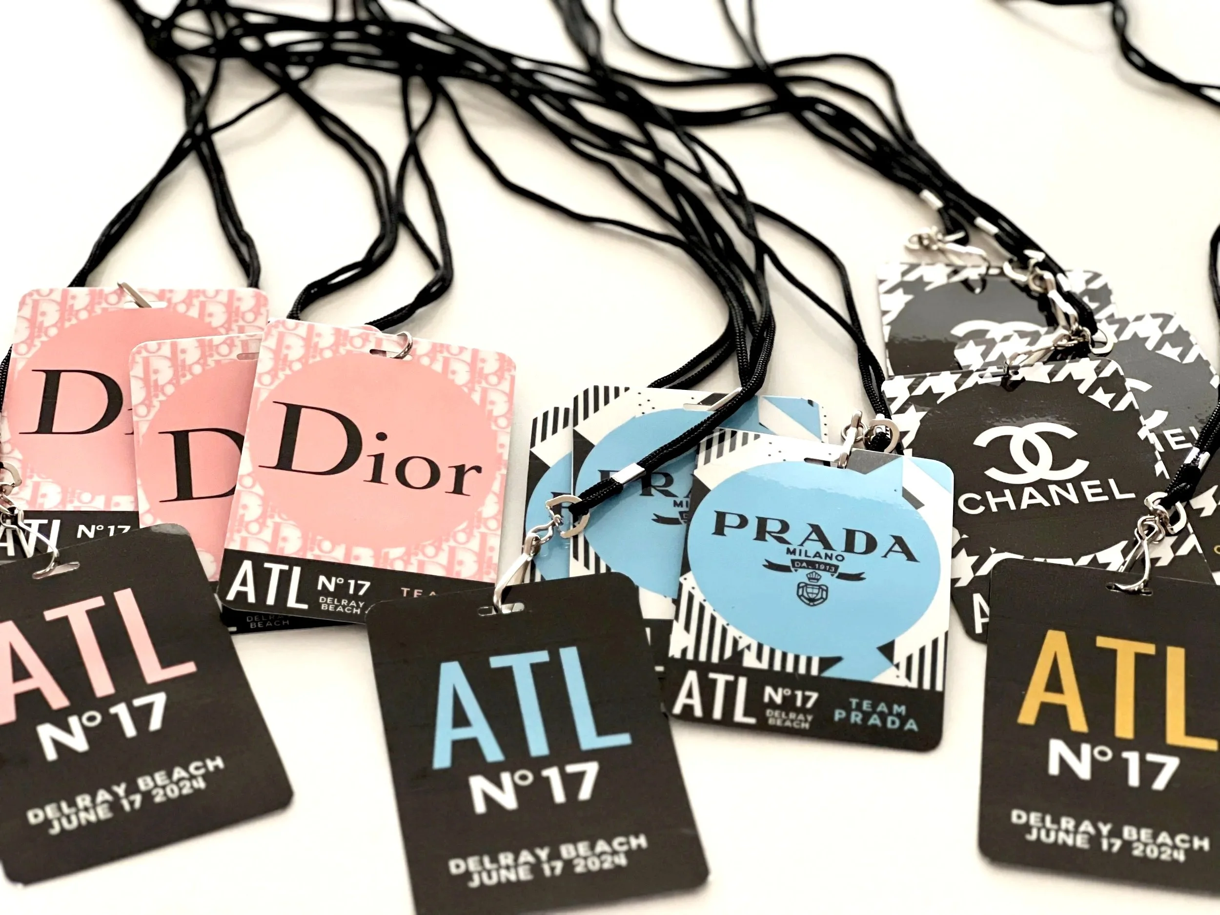 Collection of event badges with black, pink, blue, and black and white designs, displaying the text 'ATL,' 'Delray Beach,' and the date June 17, 2024, attached to black lanyards.