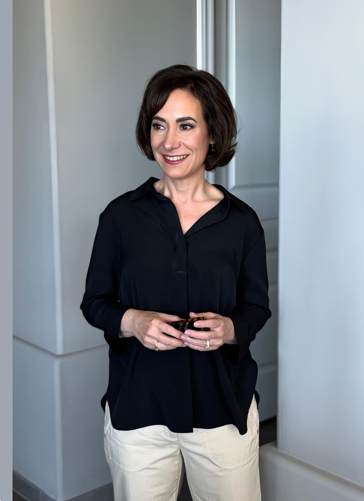 Ninette Hupp wearing a black shirt and beige pants, standing indoors near a white wall and doorway.