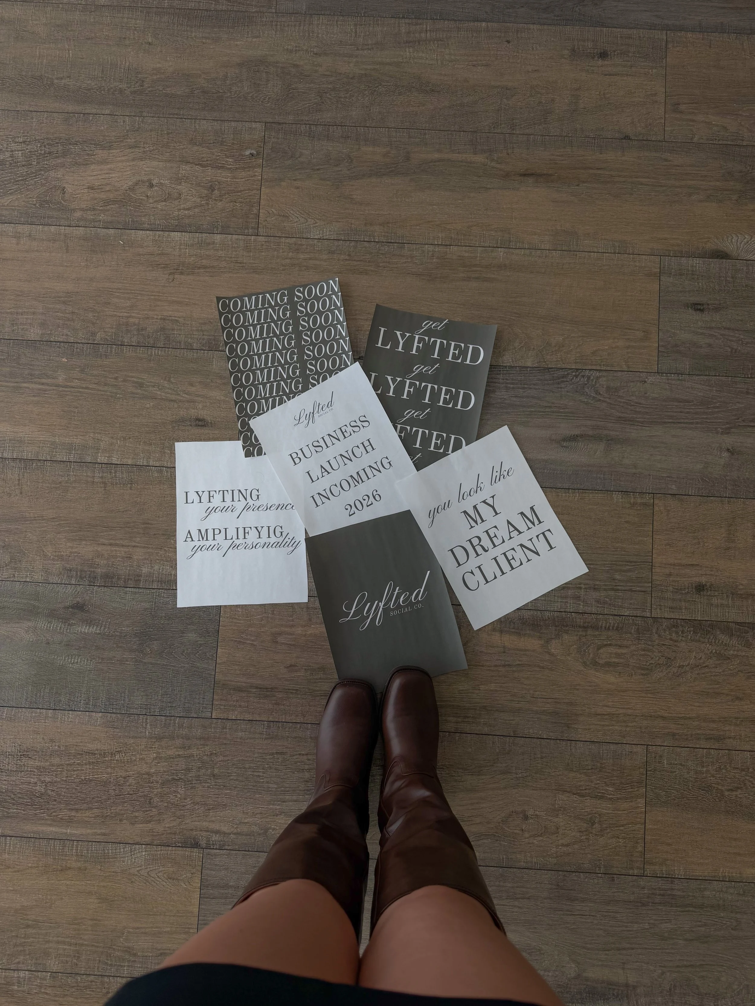 Person standing on a hardwood floor, wearing brown boots and shorts, with several printed paper sheets spread out on the floor.