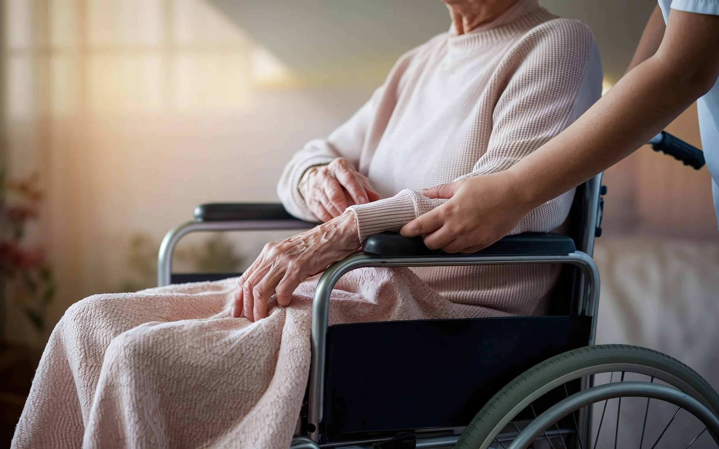 Een persoon in een rolstoel krijgt ondersteuning van een verzorger die de arm vasthoudt.