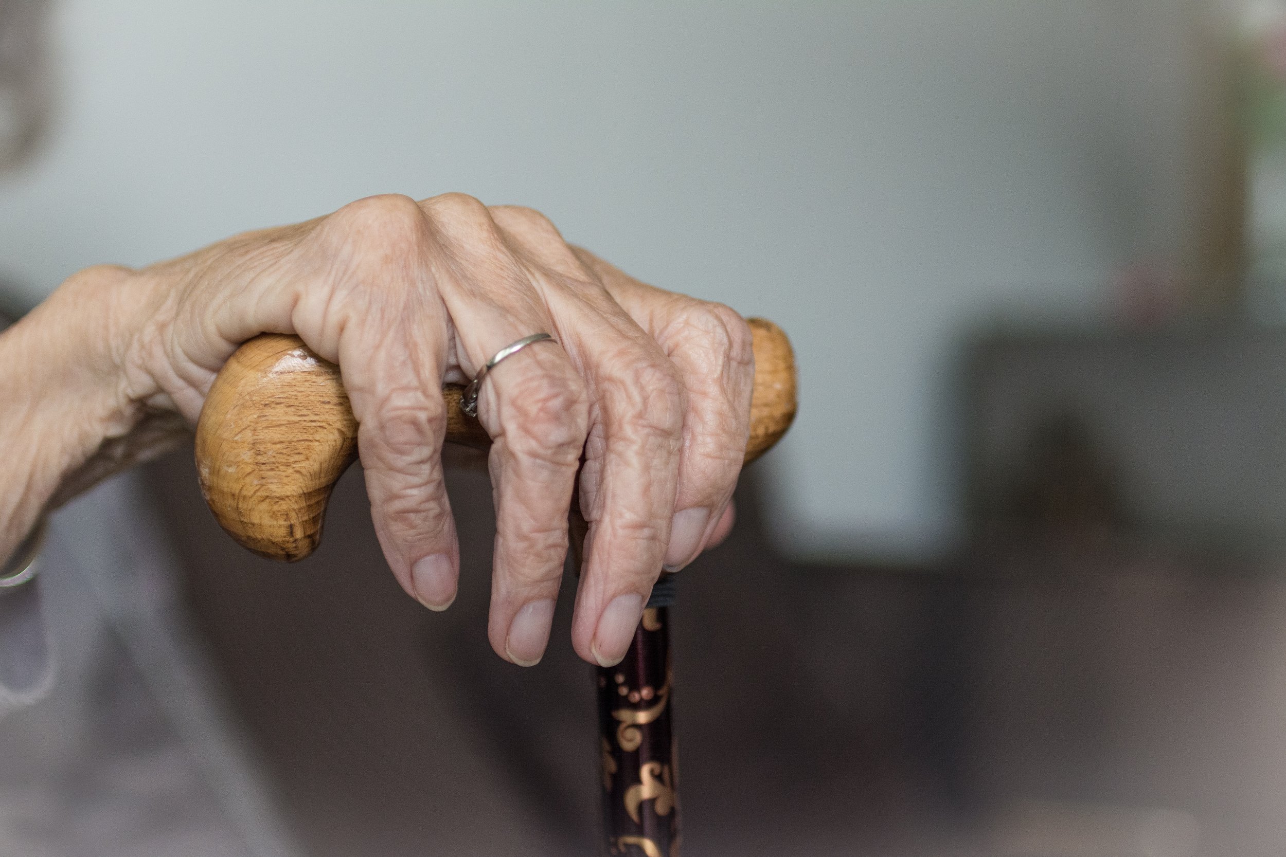 Een close-up van een oude hand die rust op een houten wandelstok.