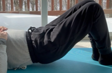 Person lying on their back on a blue exercise mat, performing a hip bridge exercise