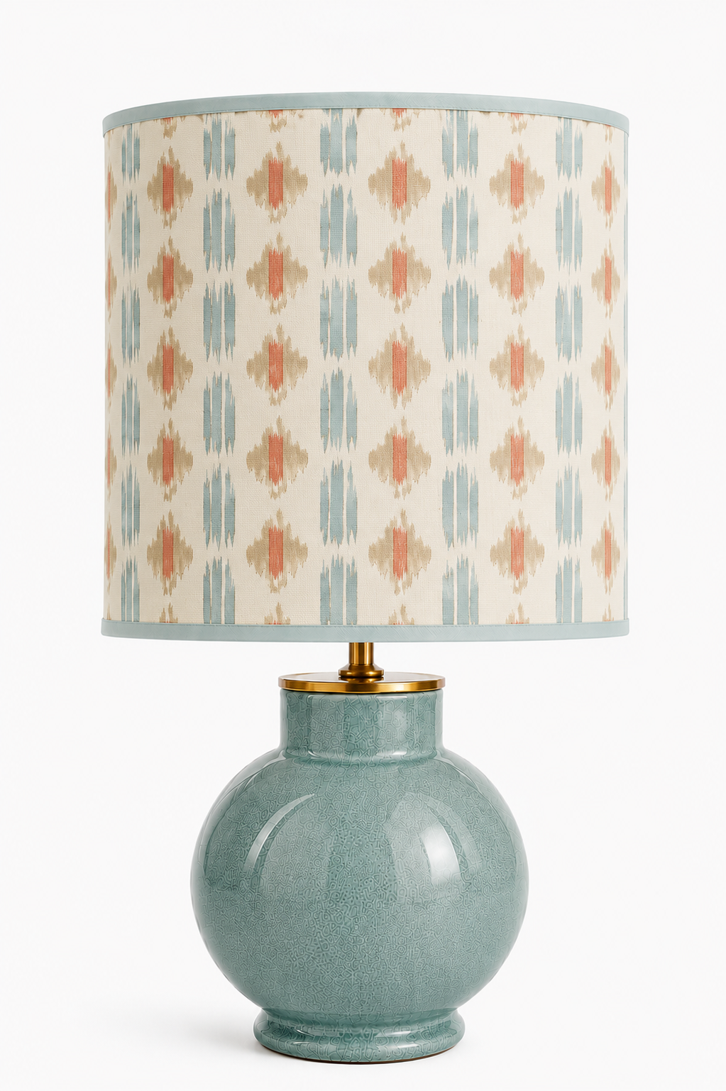 Eine Tischlampe mit einem großen, runden, grünen Keramik-Fuß und einem Textilmantel mit buntem, geometrischem Muster in Beige, Blau und Rot.