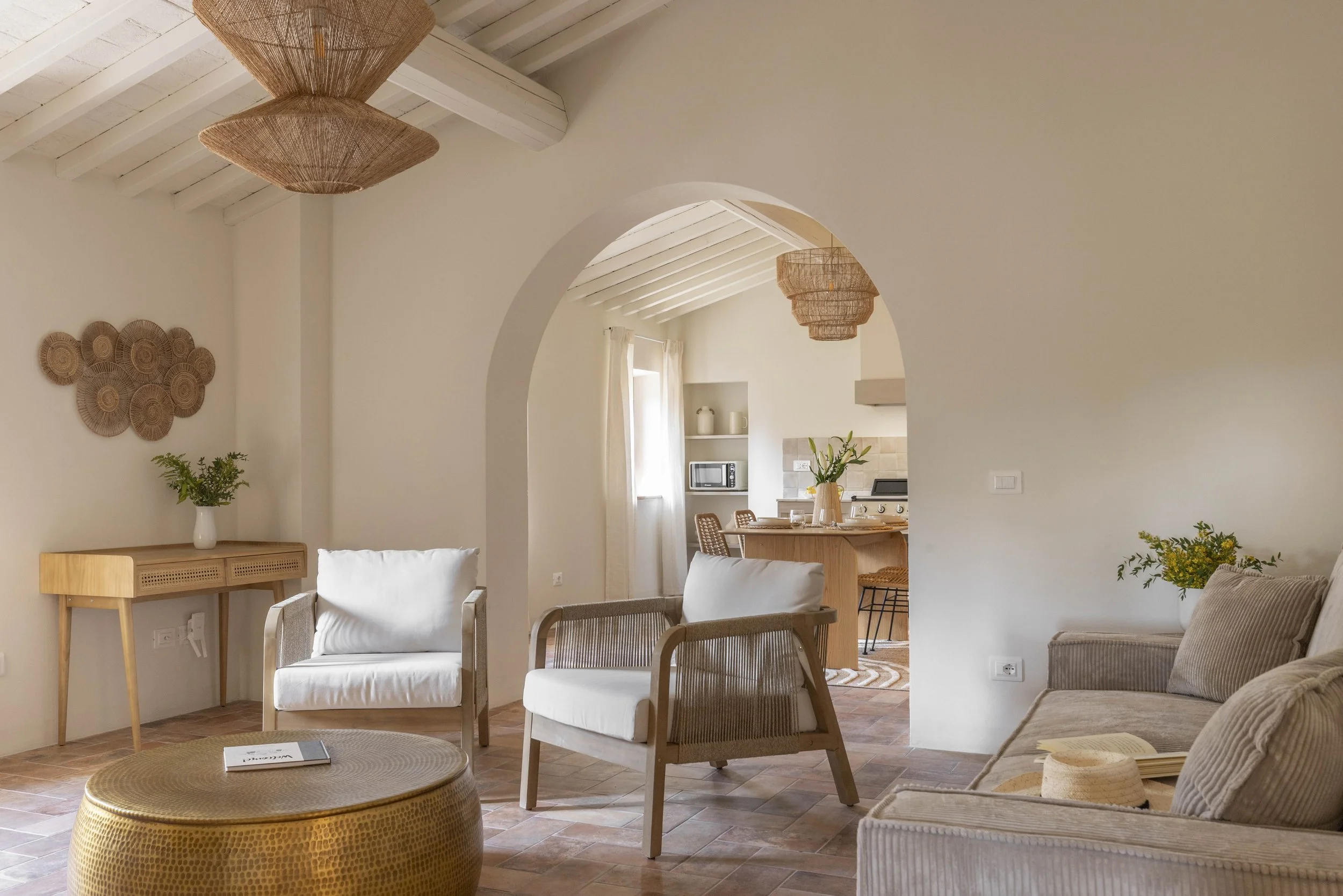 Inquadratura del salotto dell'appartamento Casa per il Pozzo a Lajatico. Un salotto dallo stile moderno e cosy, decorata con artigianato in paglia e piante verdi, con soffitto a travi bianche e lampade di vimini.