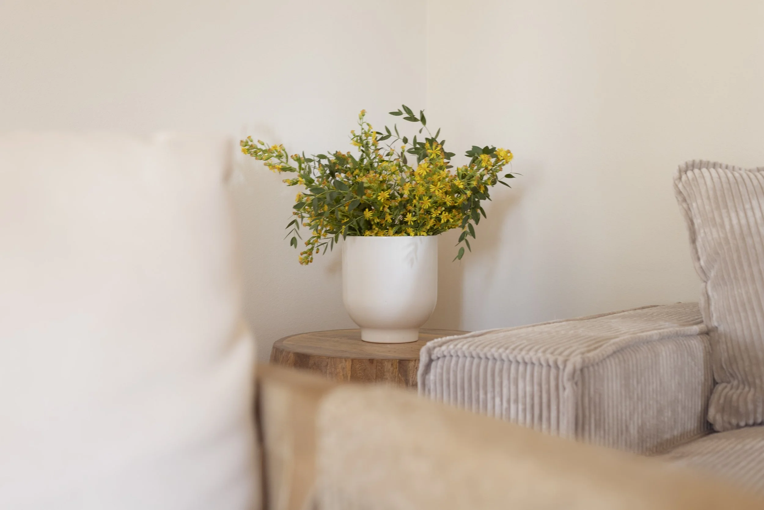 Dettaglio dal salotto dell'appartamento di Casa per il Pozzo a Lajatico.  Vaso bianco con fiori gialli e foglie verdi su un tavolo di legno.
