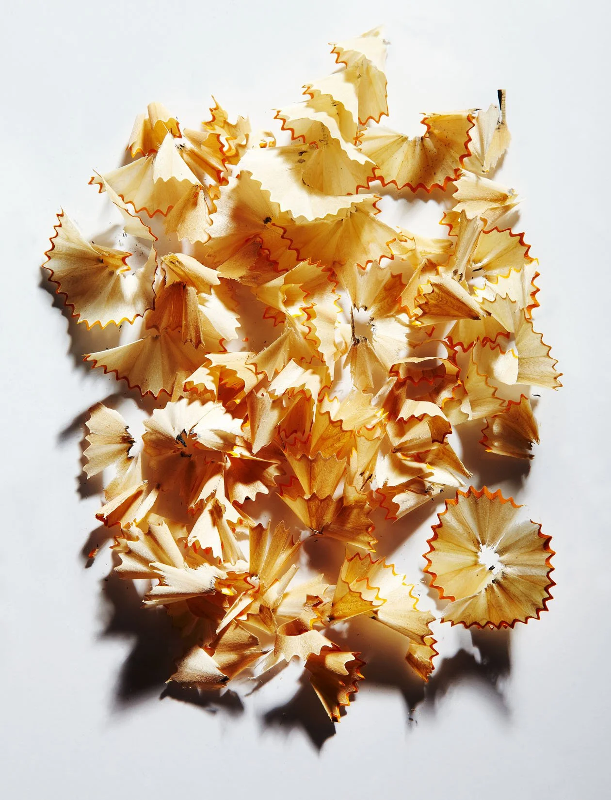 A scattered pile of yellow pencil shavings with red edges on a white surface.