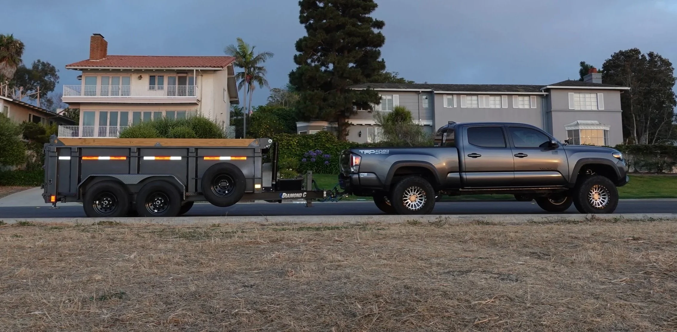 A South Bay dumpster rental and junk hauling truck towing a large utility trailer down a residential neighborhood street.