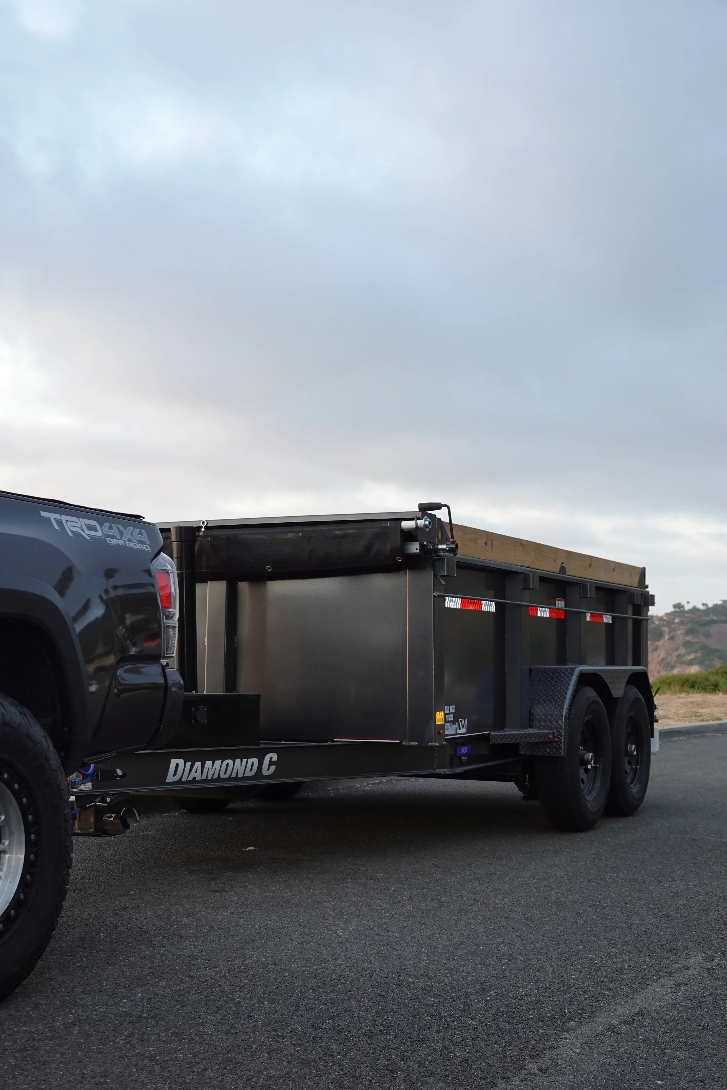 A black pickup truck and trailer setup used for junk hauling and trash removal, parked on the side of a road.