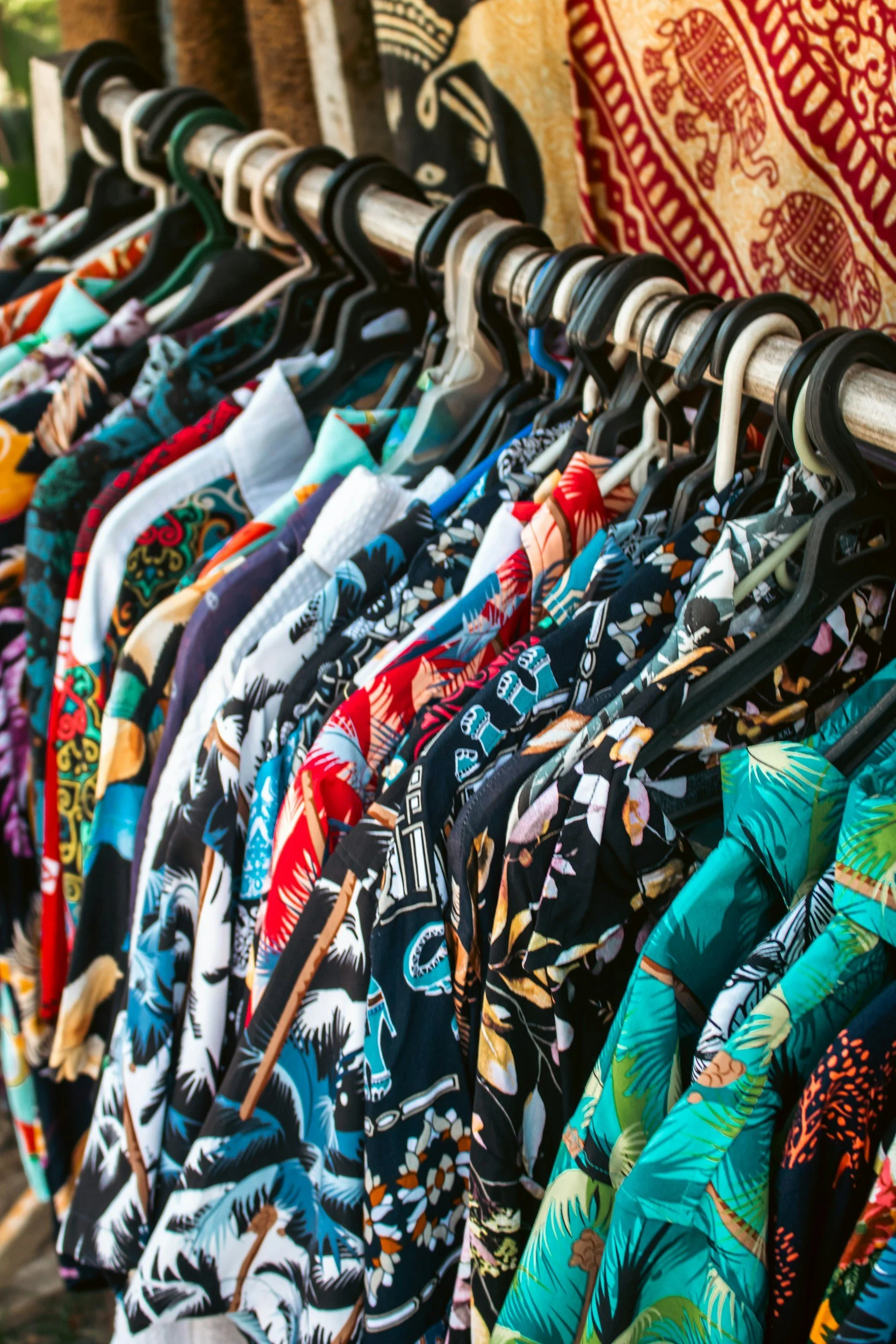 Colorful Hawaiian shirts hanging on a clothing rack at a market or store.