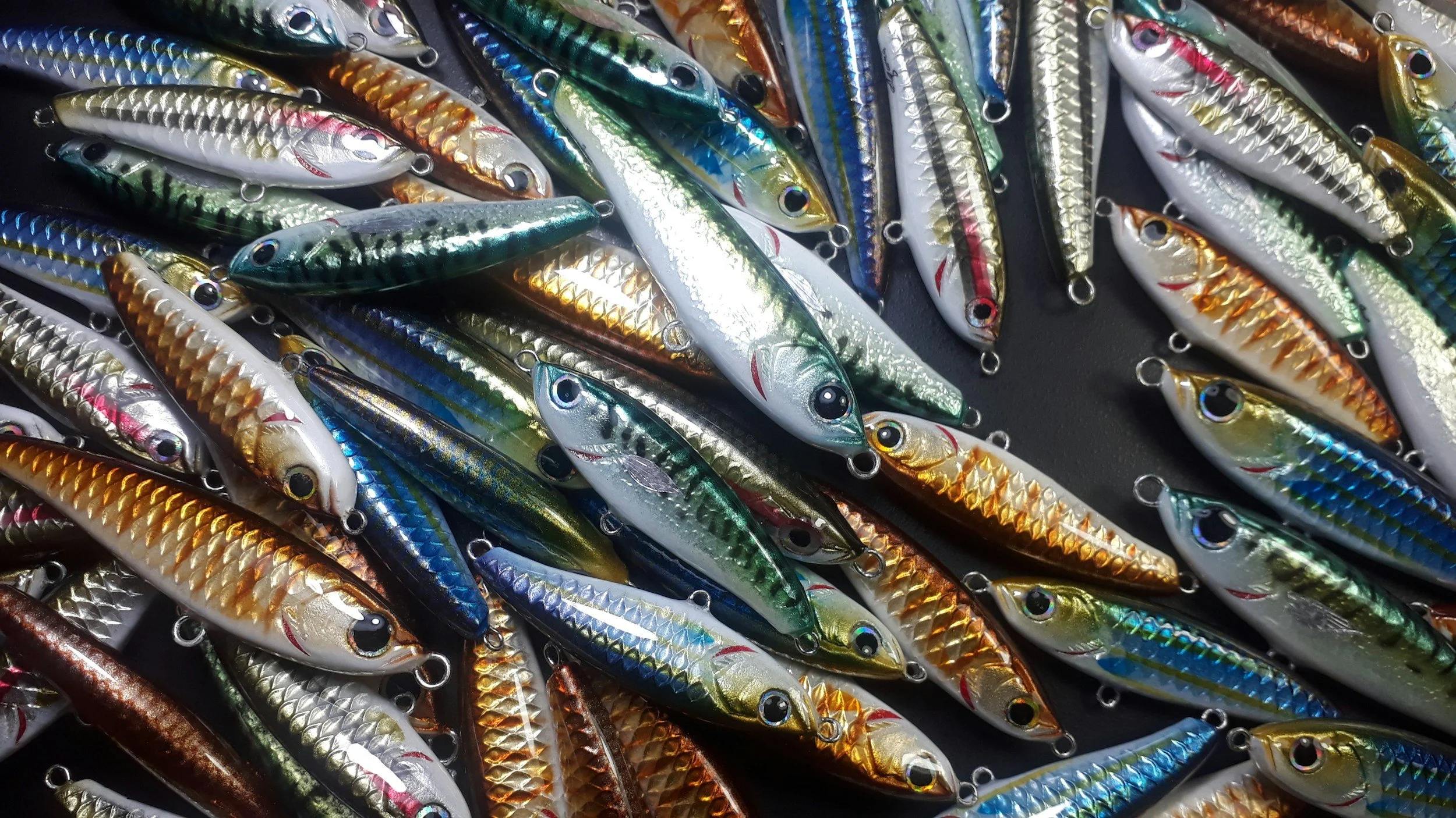 A pile of colorful fishing lures shaped like small fish with shiny, reflective bodies and hooks.