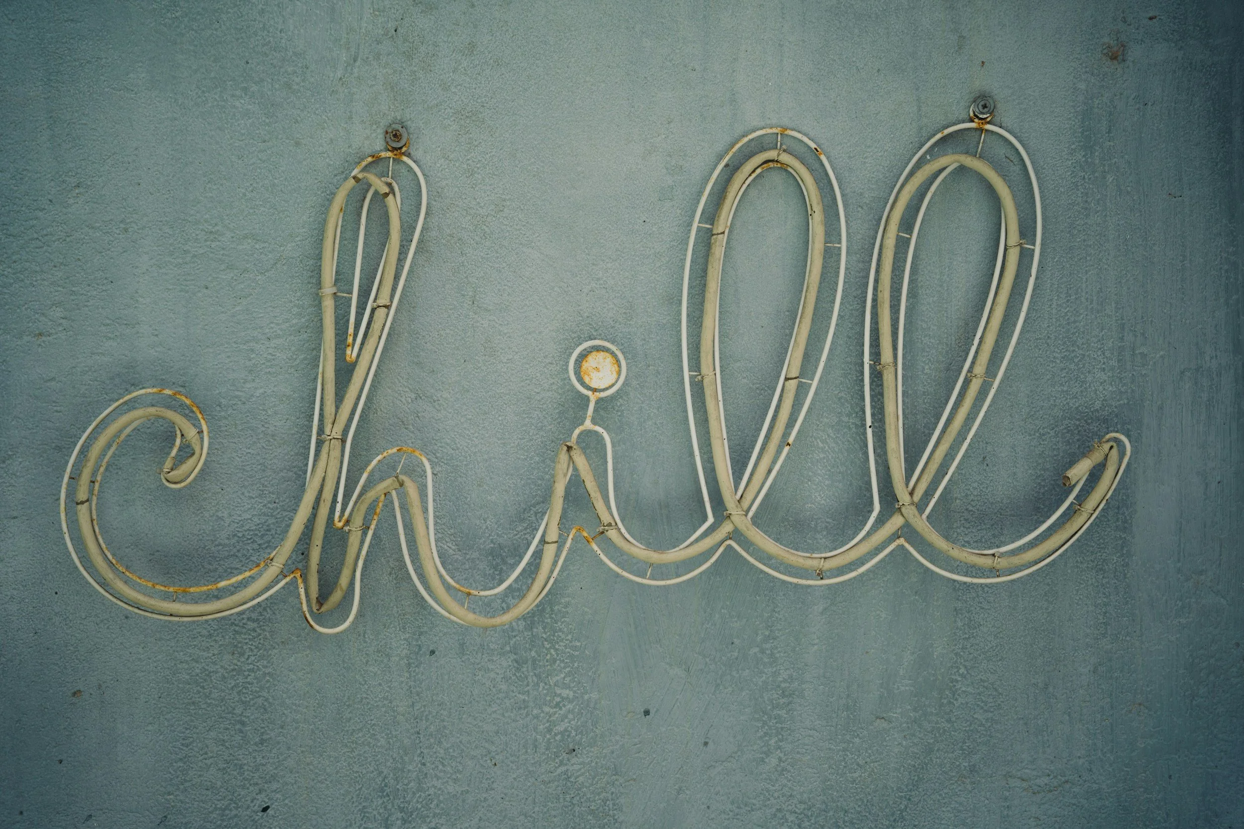 A weathered neon sign with the word 'love' in cursive, mounted on a textured gray wall. The sign has rust spots and appears old.