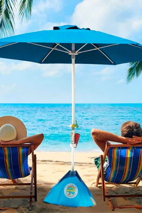 People relaxing on beach chairs under a large blue beach umbrella by the ocean.