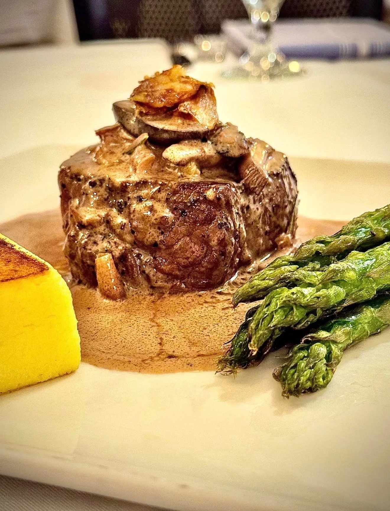 A plated meal featuring a medium-rare steak topped with sautéed mushrooms, with grilled asparagus and a wedge of lemon on the side, all on a white plate.