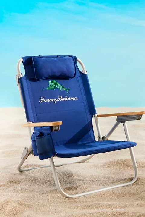 A blue Tommy Bahama beach chair on the sand with a blue sky background.