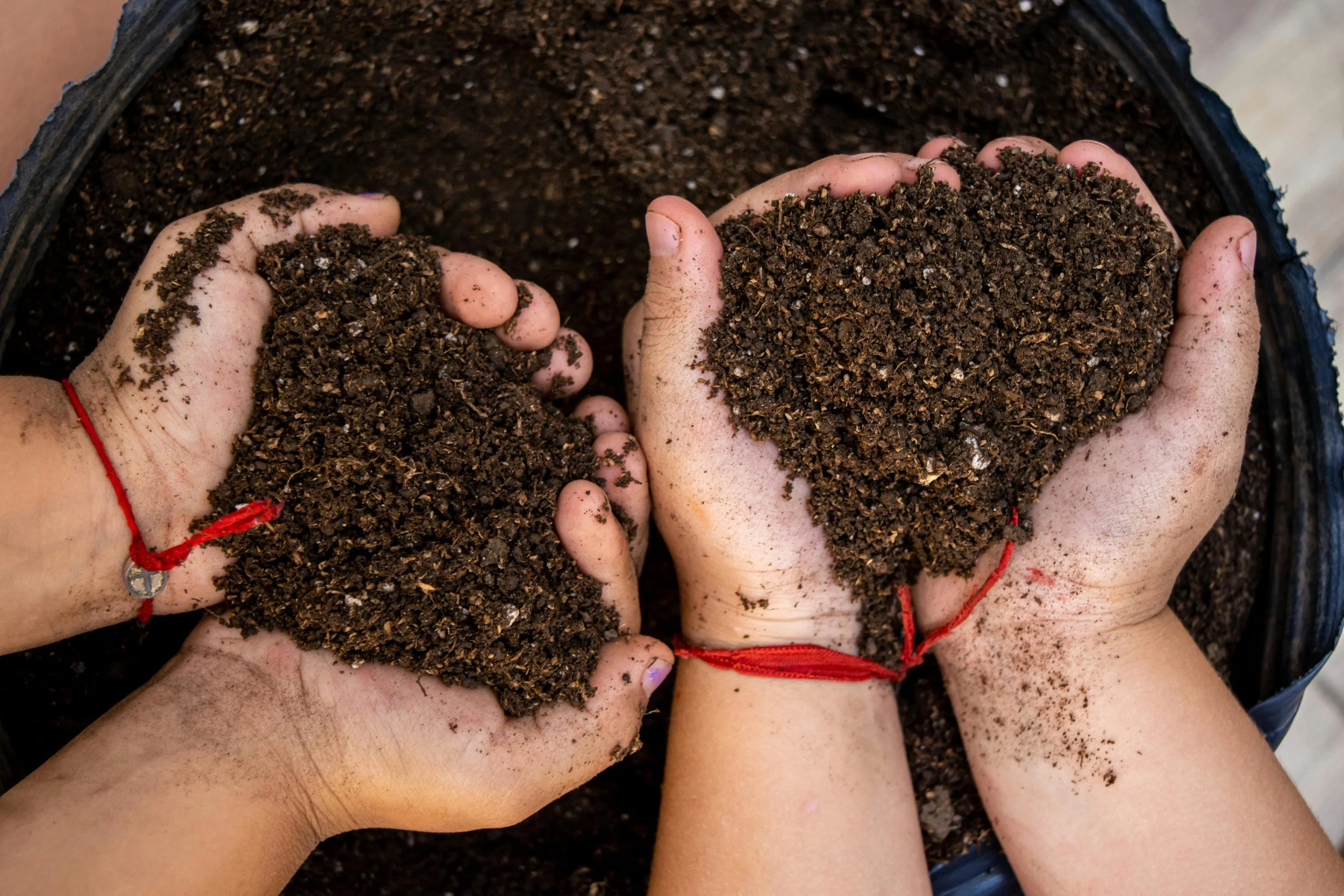 Multiple hands holding dark, crumbly soil in a bucket.