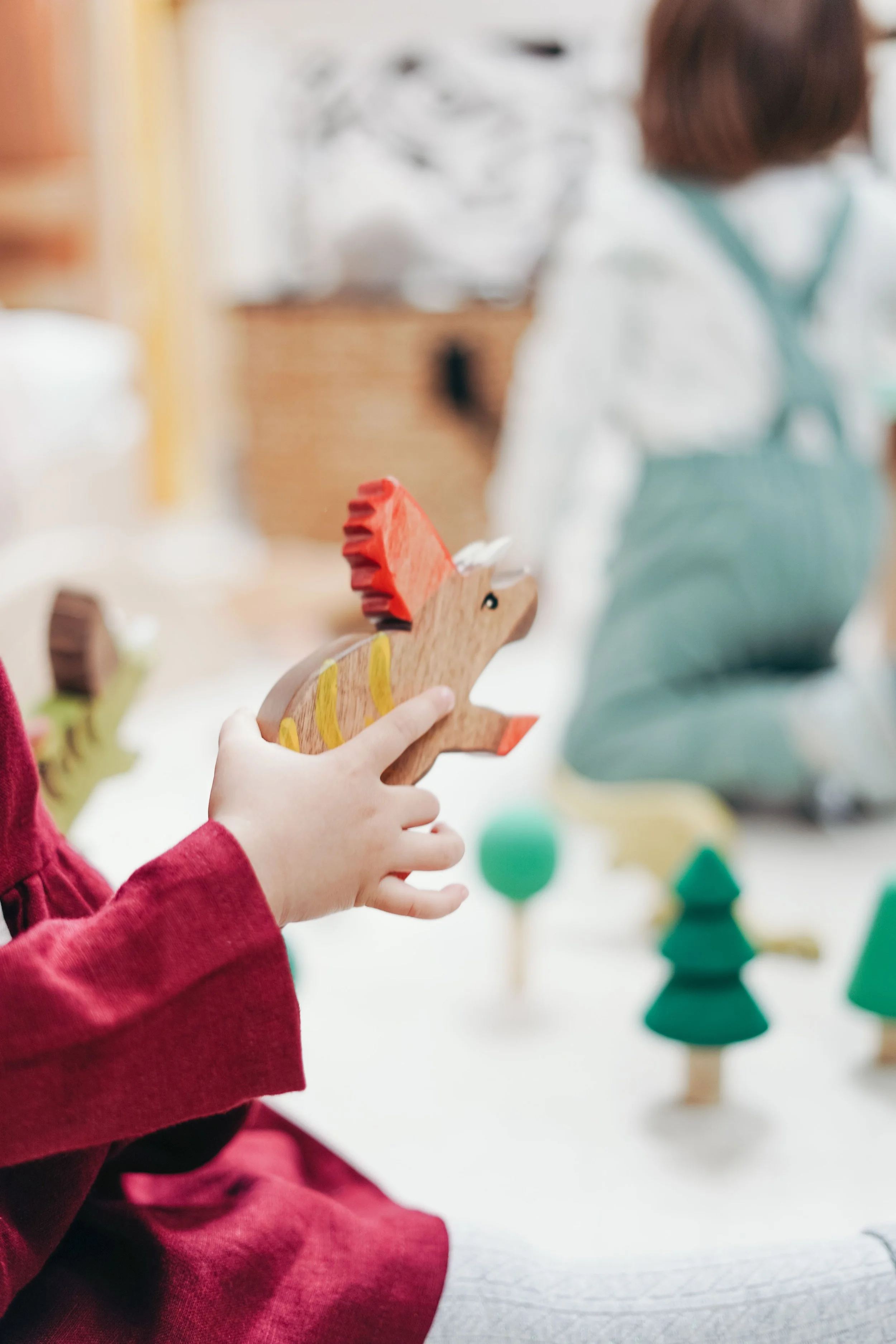 A child holding a wooden dinosaur toy in a colorful playroom.