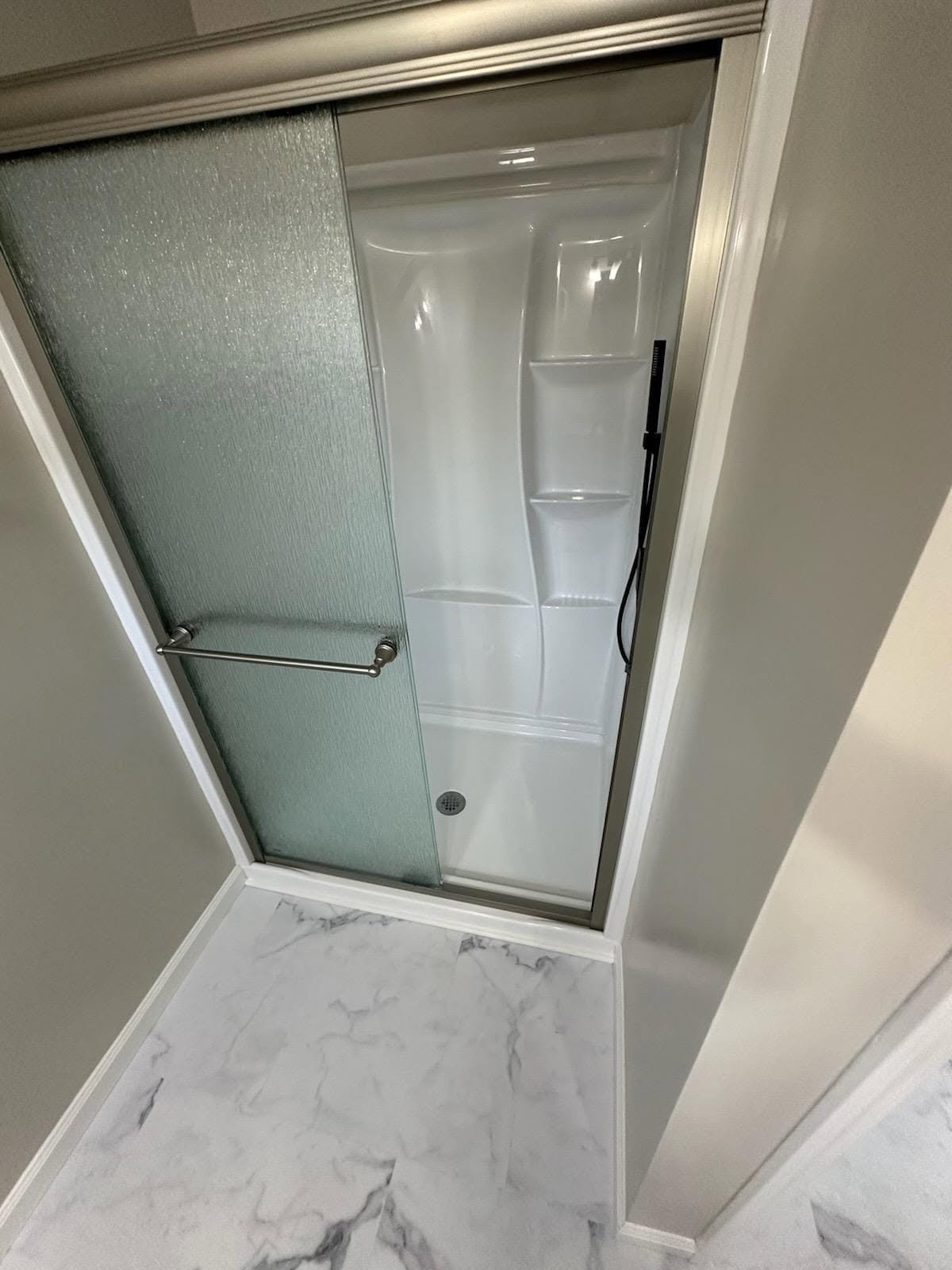 Shower stall with frosted glass sliding door, built-in shelves, and handheld showerhead.