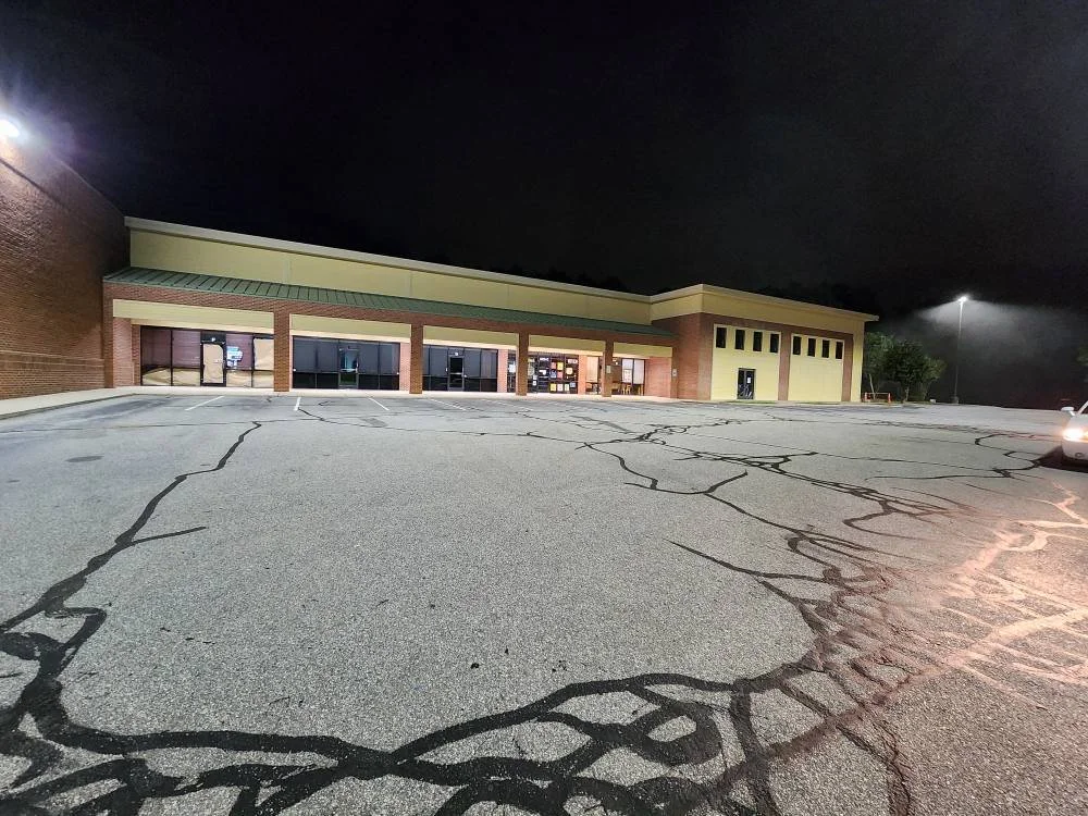 any property renovations Empty parking lot outside a storefront at night with visible cracks in the pavement.