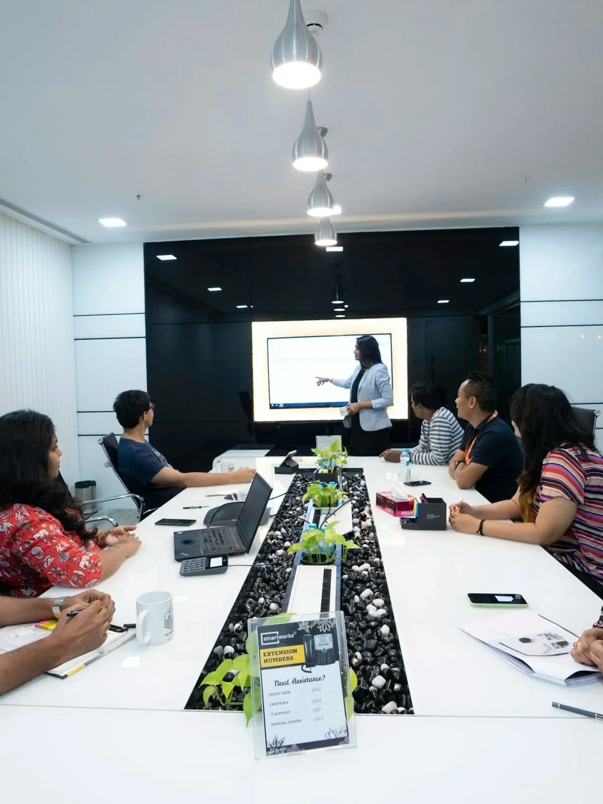 Business meeting in a conference room with a woman giving a presentation to a group of diverse seated professionals.