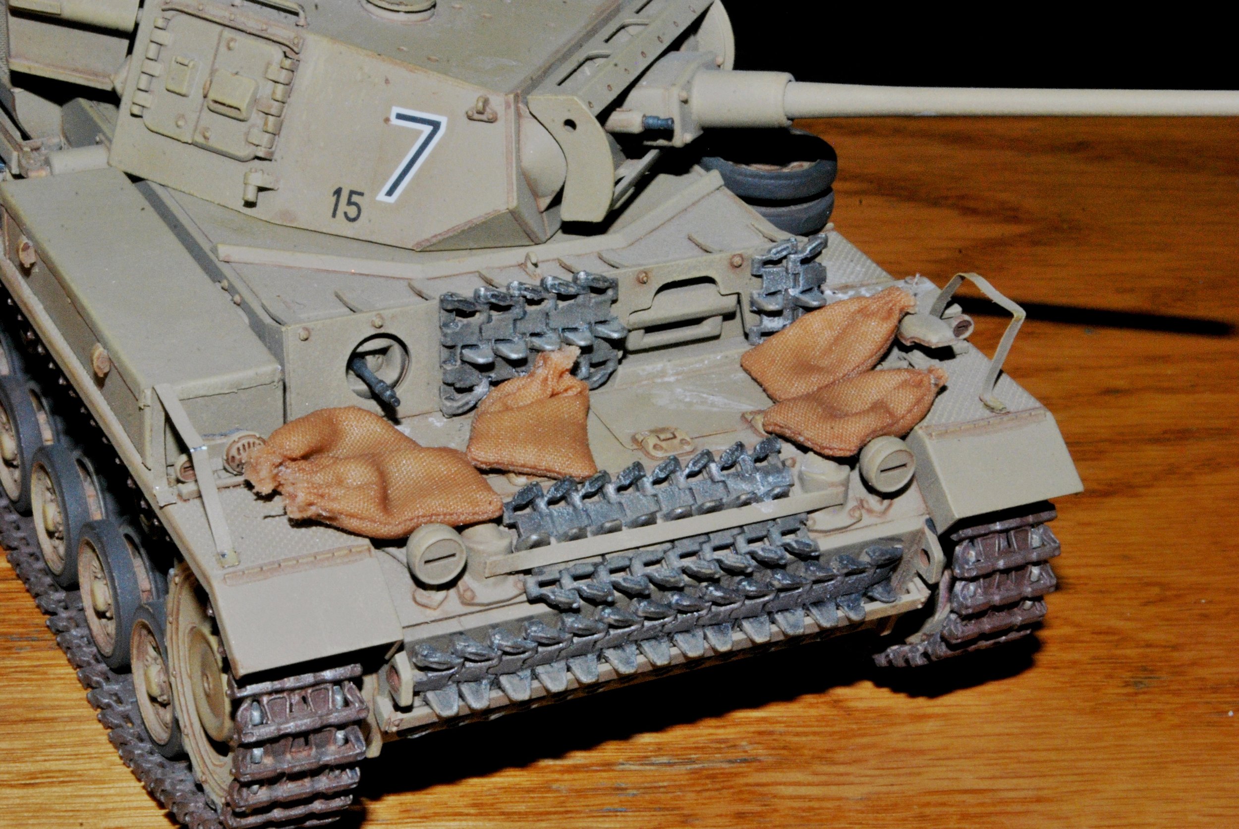 Close-up of a detailed scale model of a tan military tank with sandbags on the front of the hull
