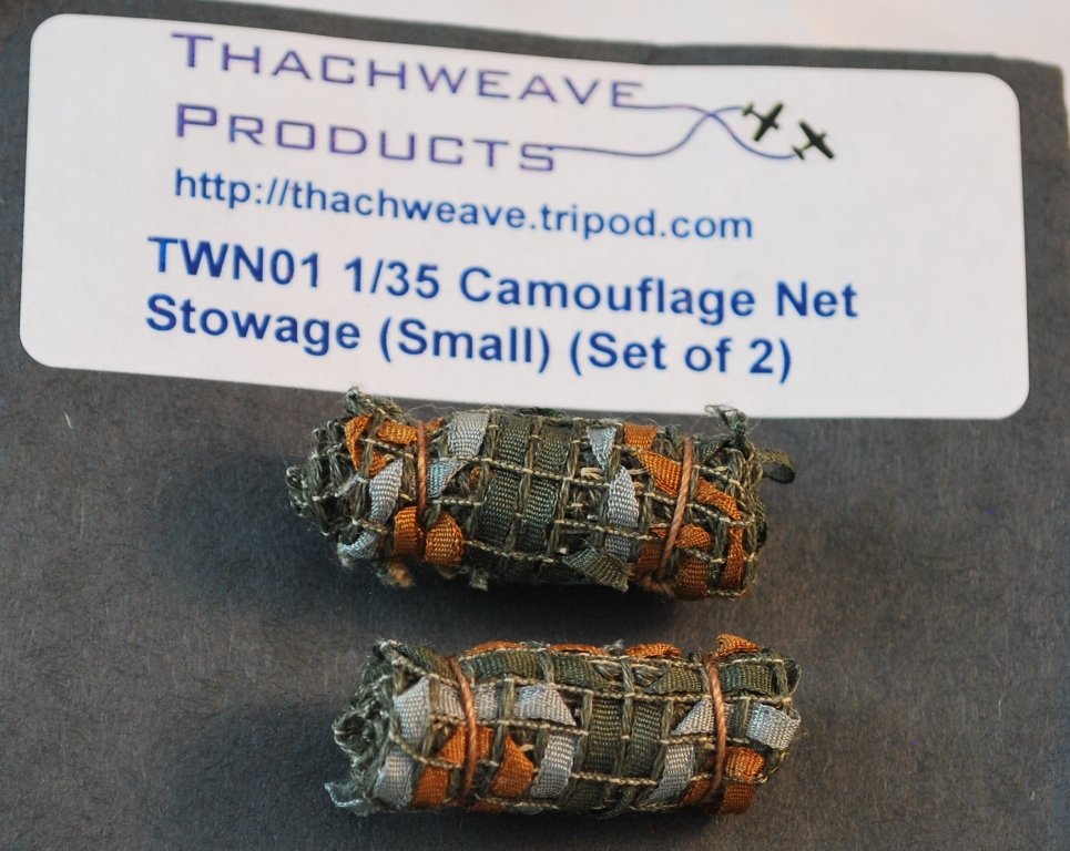 Two small, rolled camouflaged netting pieces with a grid of crossed orange and gray elastic bands, placed on a black surface with a label above them.