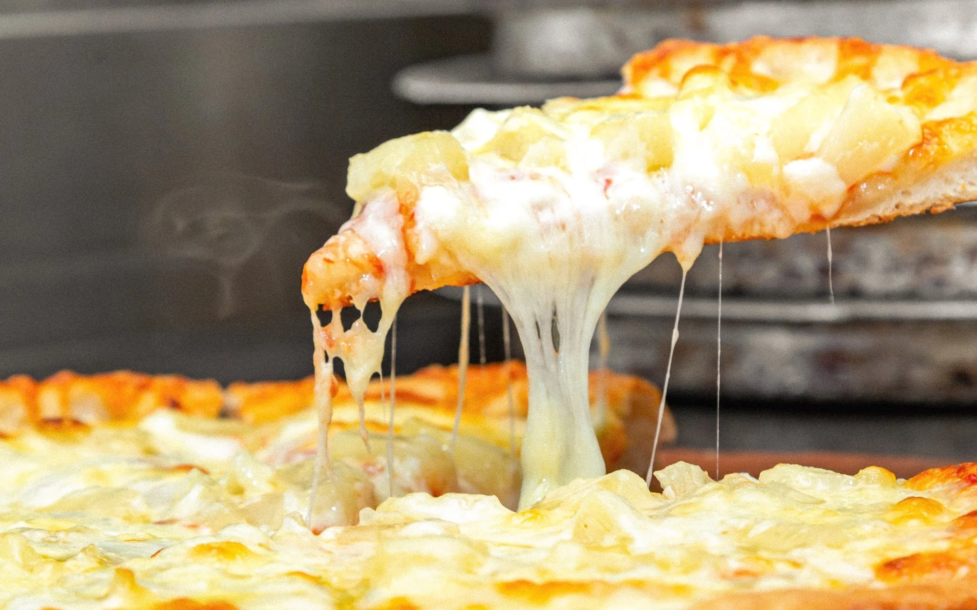 Close-up of a slice of cheese pizza with melted cheese stretching from the slice.