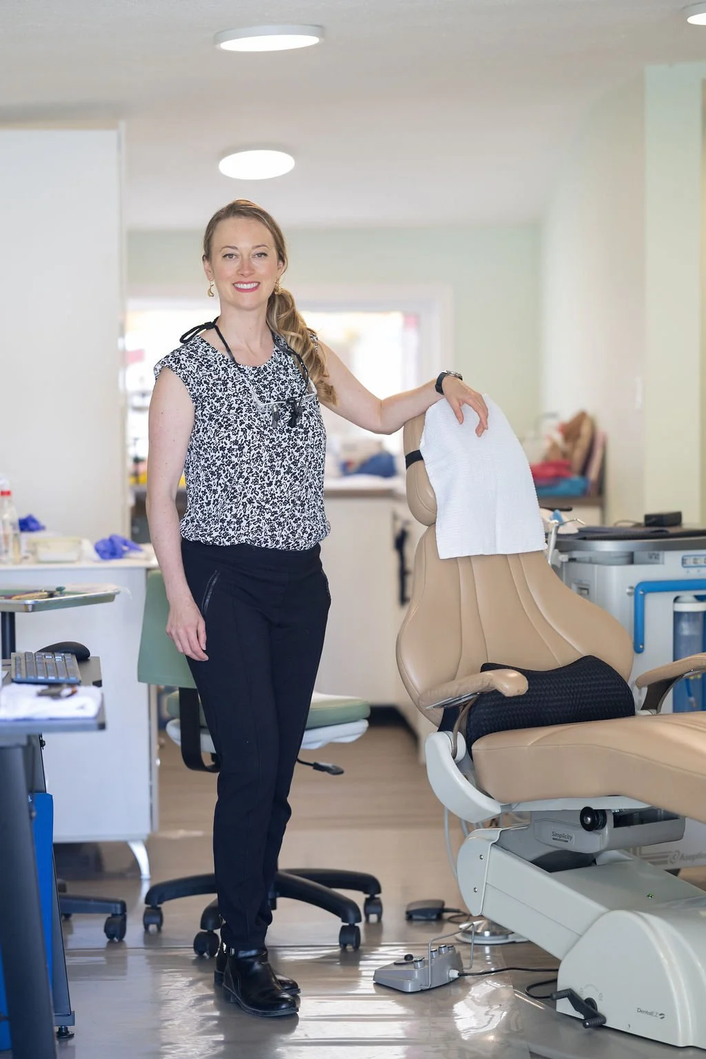 Female healthcare professional standing beside a dental chair in a clinic or hospital setting.